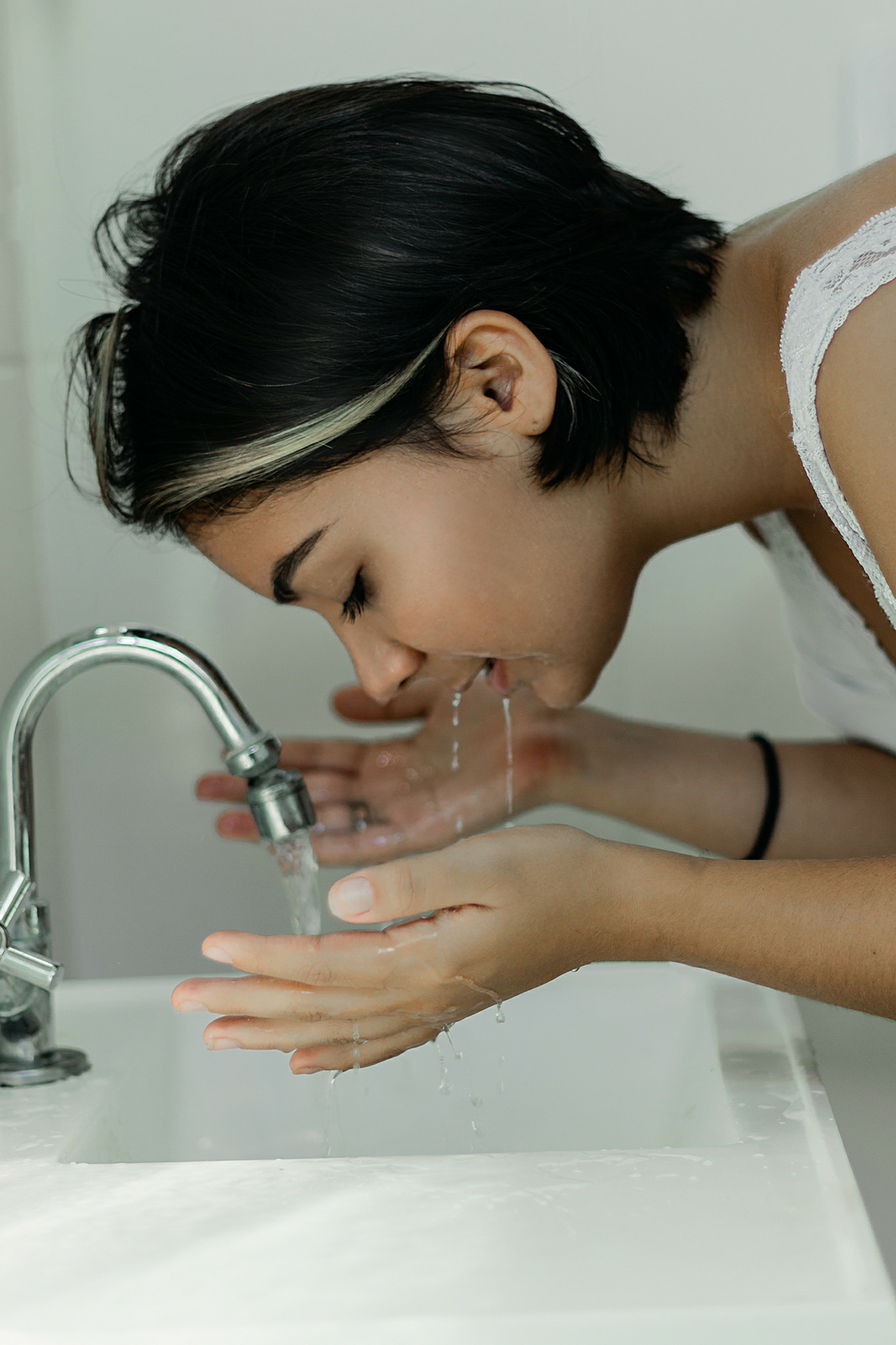 A woman washing her face with water at a bathroom sink