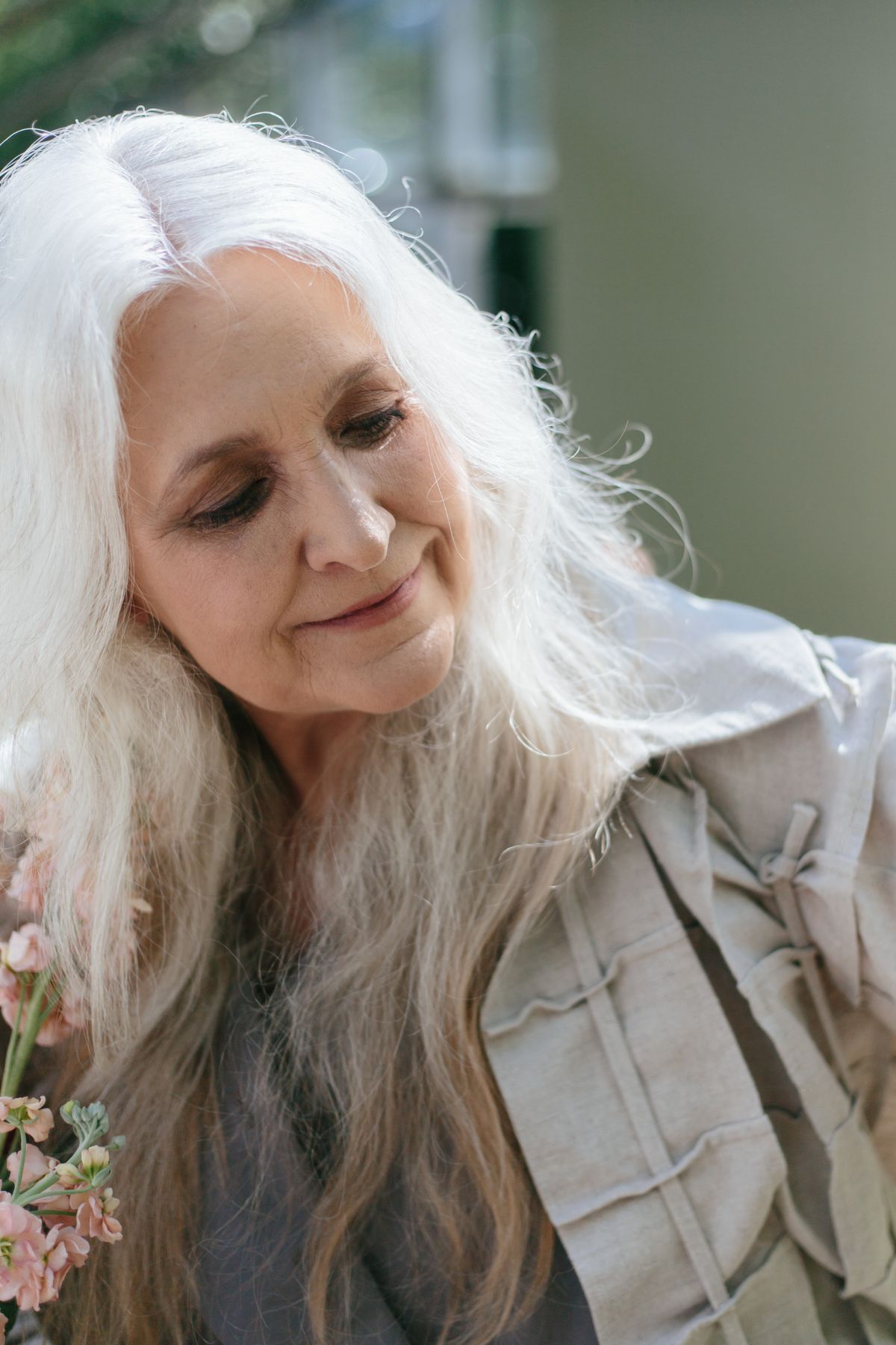 A smiling older woman with long gray hair holding flowers