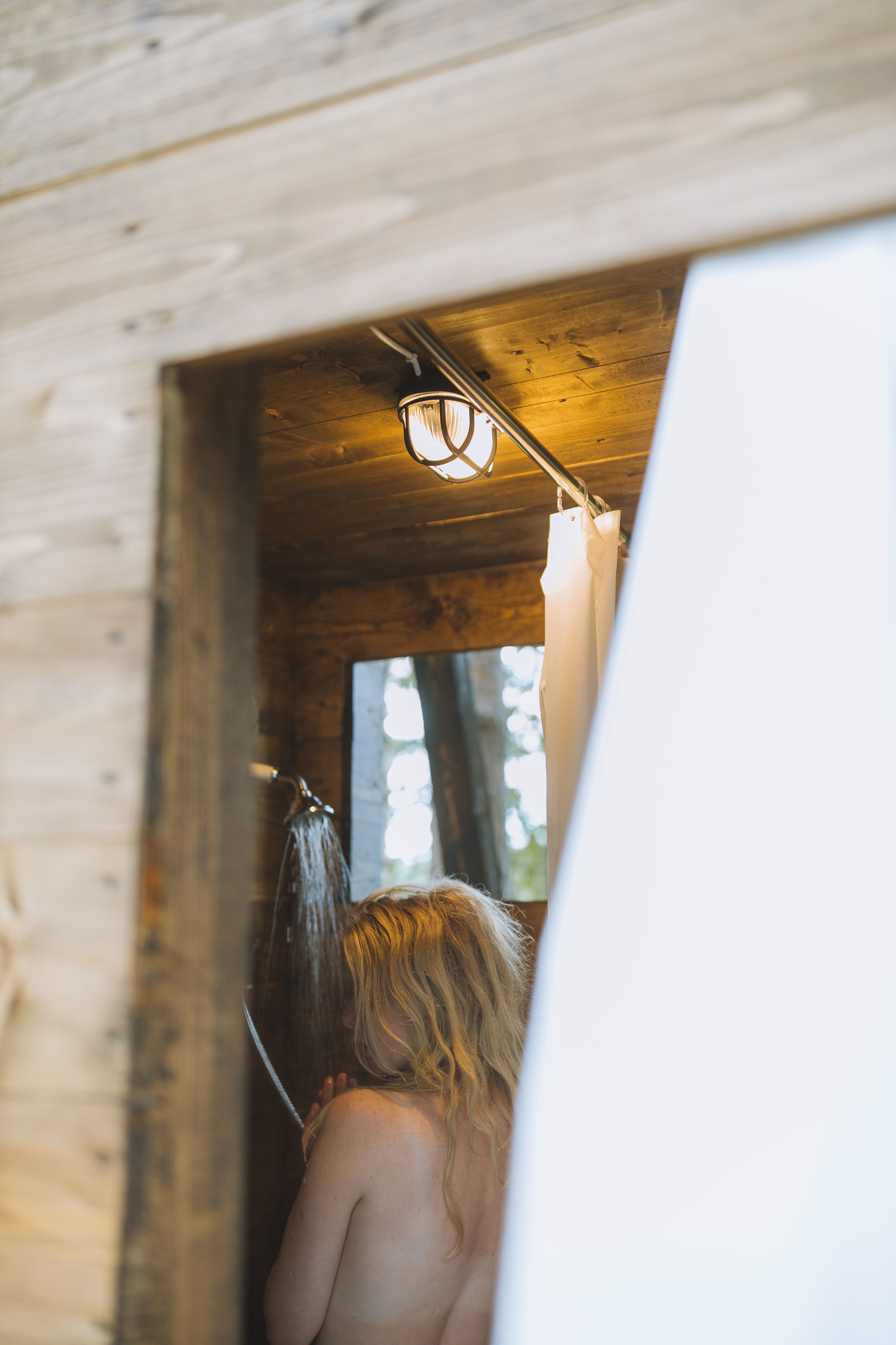 A woman taking a shower in a softly lit wooden bathroom